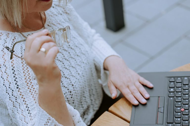 Ingrid Angelika Müller Eine Person mit einem Laptop, die am Tisch sitzt und nachdenklich mit einem Stift spielt.